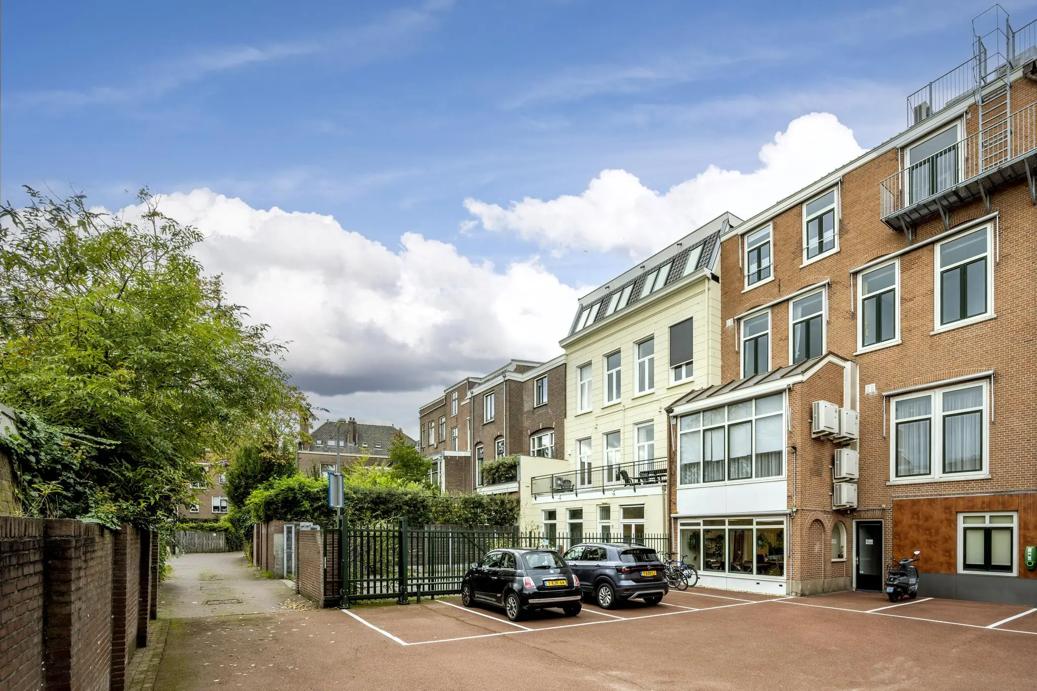 Achterzijde van een rij herenhuizen aan de Nieuwe Gracht met een omheinde parkeerplaats en geparkeerde auto's.